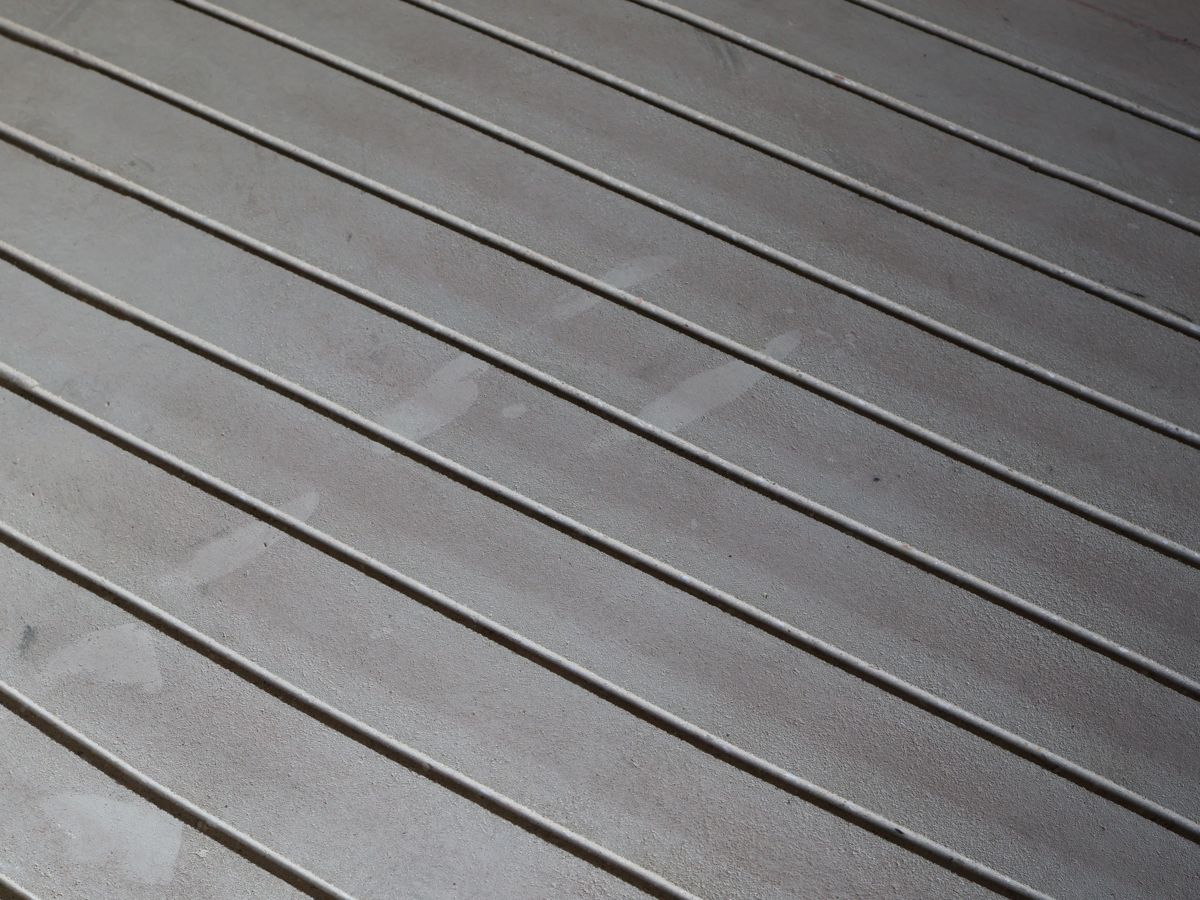 Frisch gefräste, abgesaugte parallele Kanäle in einem grauen Estrich, schräg von oben fotografiert.