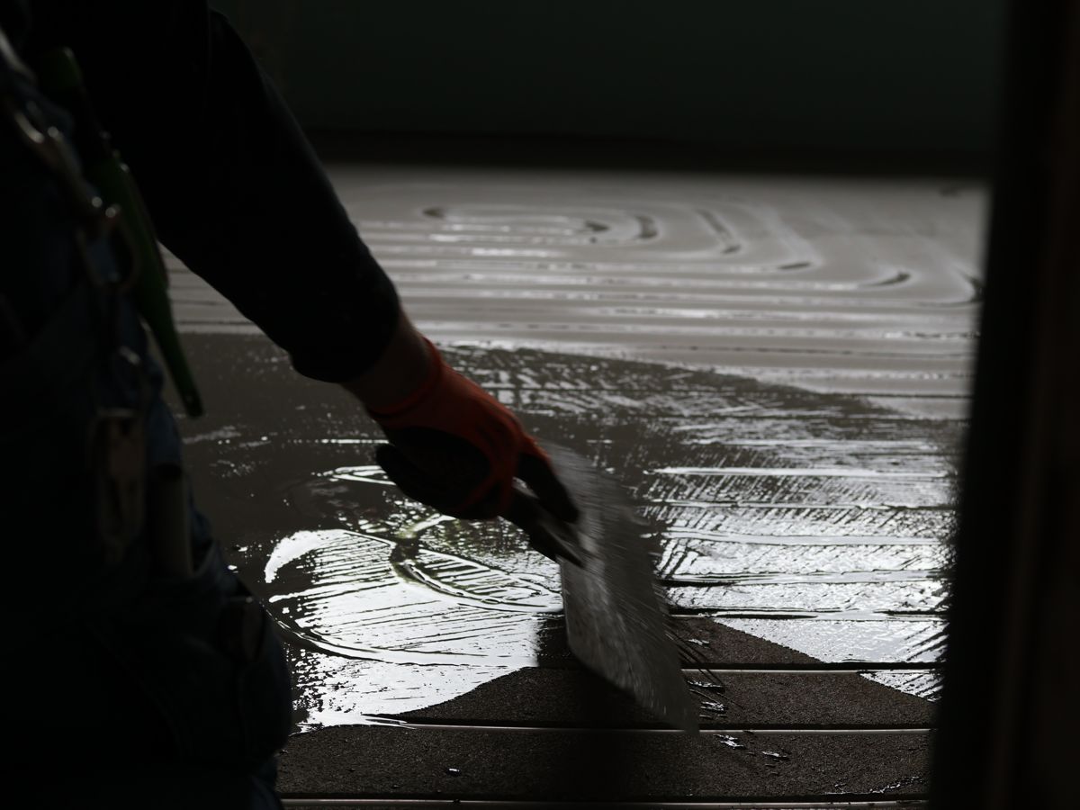 Handwerker zieht frisch eingebrachten, flüssigen Rohrverschluss mit einer Flitsche über die Fräskanäle ab.